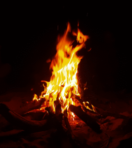 A solitary bonfire glowing brightly in the darkness, its flames dancing against a black night background.